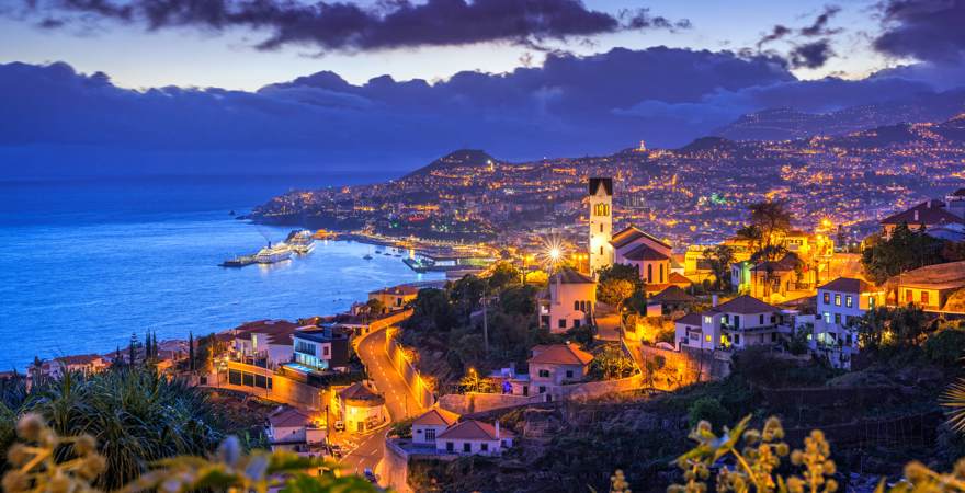 Madeiras Hauptstadt Funchal bei Nacht mit Meer und Bergen
