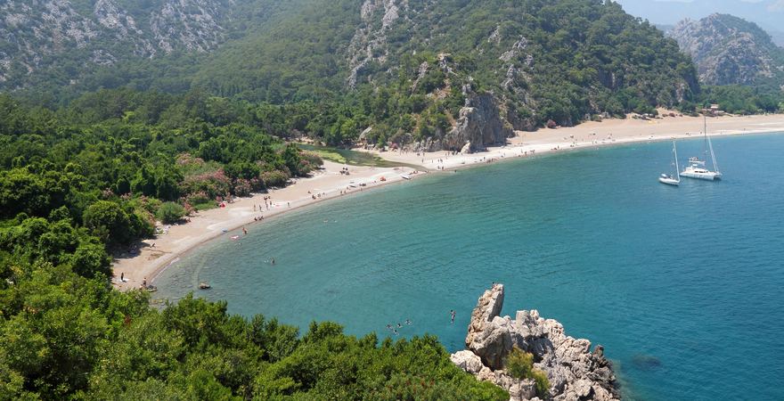 Der Strand Olympos vor dem Taurusgebirge in der Türkei mit Blick auf grüne Berglandschaft, Wald, Kiesstrand und Meer