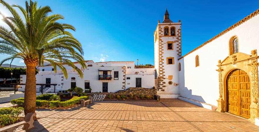 Historische Kirche im malerischen Betancuria-Dorf auf Fuerteventura, Kanaren, Spanien, umgeben von Palmen und traditionellen weißen Gebäuden