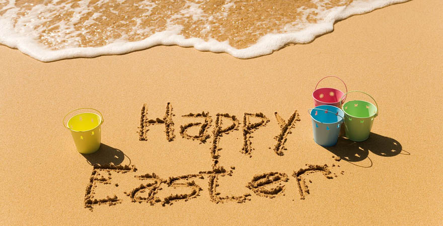 "Happy Easter" am Strand im Sand geschrieben umringt von bunten Eimern
