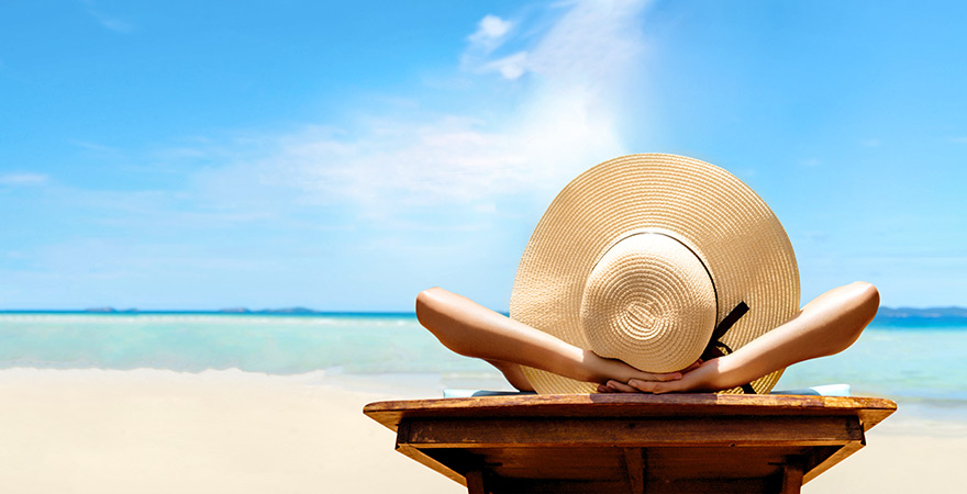 Frau mit Sonnenhut relaxt am sonnigen Sandstrand