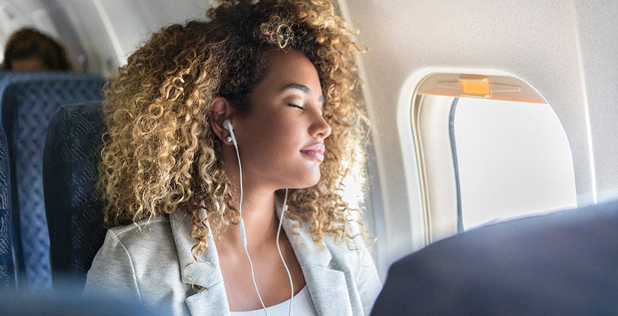 Frau entspannt mit Musik oder Podcast im Flugzeug