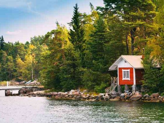 Finnland rotes Haus am Ufer mit Bäumen im Hintergrund