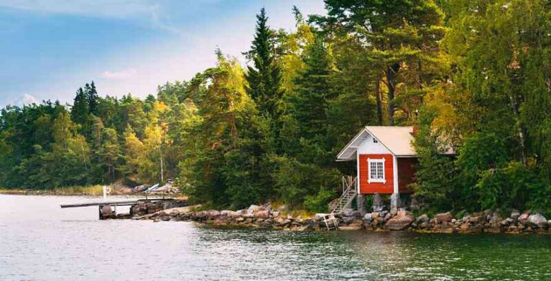 Finnland rotes Haus am Ufer mit Bäumen im Hintergrund