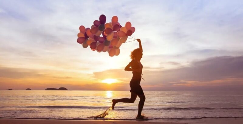 Glückliche Frau am Strand zum Sonnenuntergang mit Luftballons