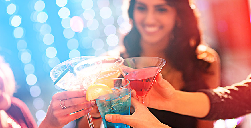 Vier Hände stoßen mit bunten Cocktails an