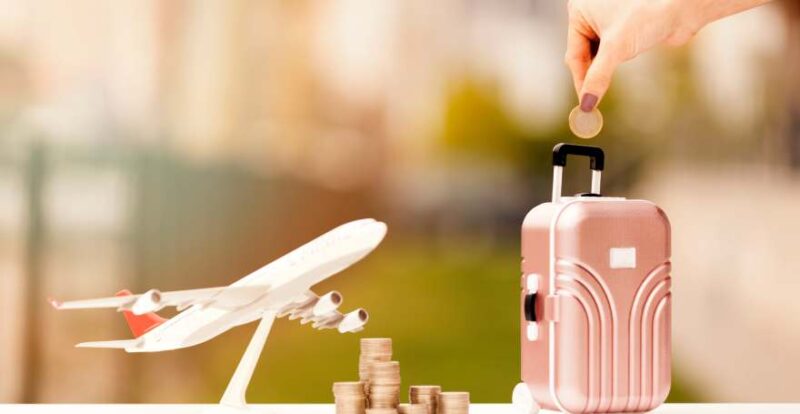 Hand mit Geldmünze, Mini-Koffer und Mini-Flugzeug