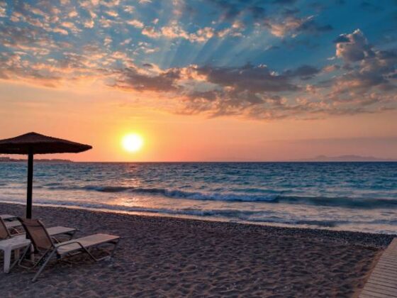 Strand auf Rhodos, Griechenland, mit Liegen und Sonnenschirmen im im Sonnenuntergang