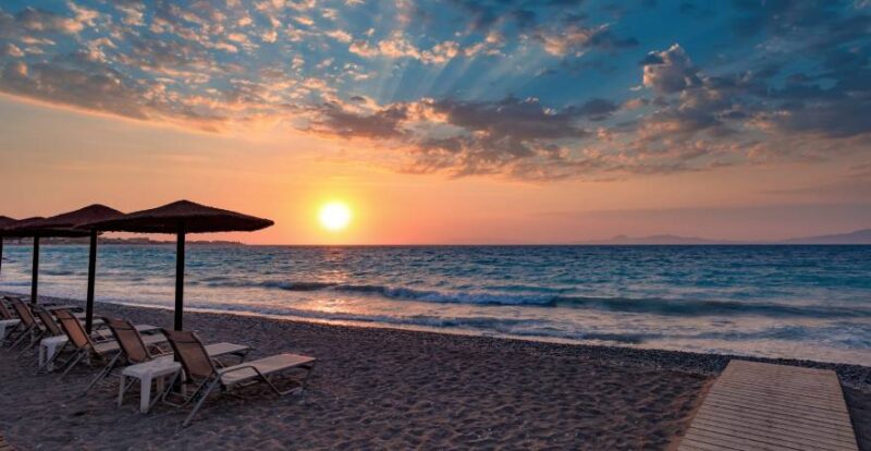 Strand auf Rhodos, Griechenland, mit Liegen und Sonnenschirmen im im Sonnenuntergang