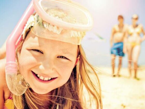 Nahaufnahme von lachendem Mädchen mit Taucherbrille und Schnorchel am Strand