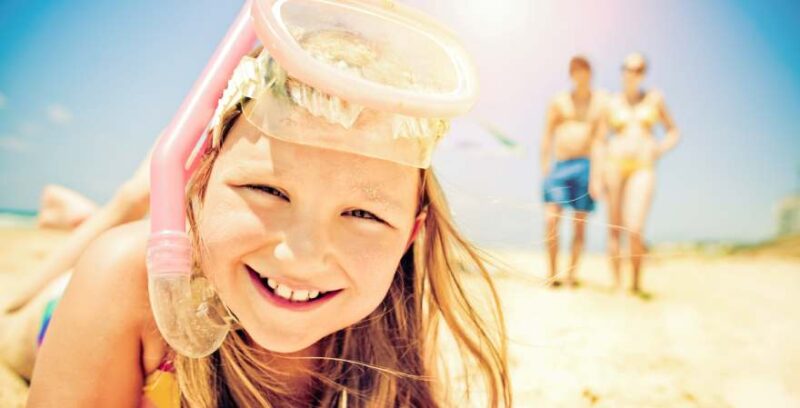 Nahaufnahme von lachendem Mädchen mit Taucherbrille und Schnorchel am Strand