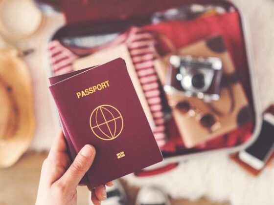 Pass in einer Hand, im Hintergrund ein offener Koffer mit Sachen