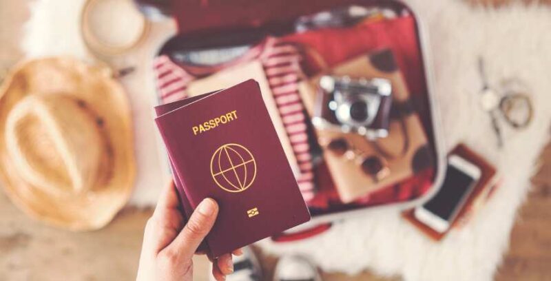 Pass in einer Hand, im Hintergrund ein offener Koffer mit Sachen