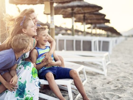 Familie mit zwei Frauen und zwei Kindern sitzt lachend auf einer Liege am Strand