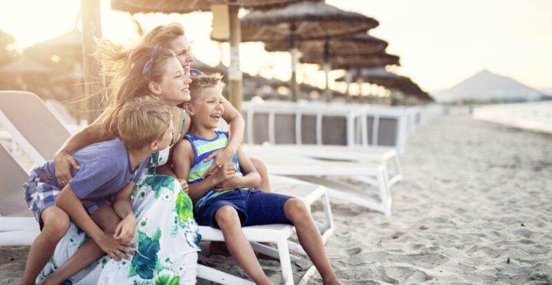 Familie mit zwei Frauen und zwei Kindern sitzt lachend auf einer Liege am Strand