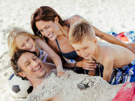 Vater, Mutter und zwei KInder lachend am Strand