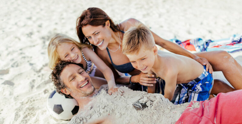 Vater, Mutter und zwei KInder lachend am Strand
