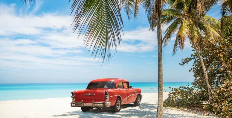 Rotes Auto unter Palmen am Strand von Kuba