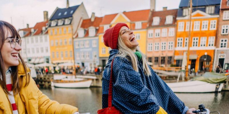 Kopenhagen Geheimtipps: lachende Frauen auf Fahrrädern vor bunten Häusern in Kopenhagen