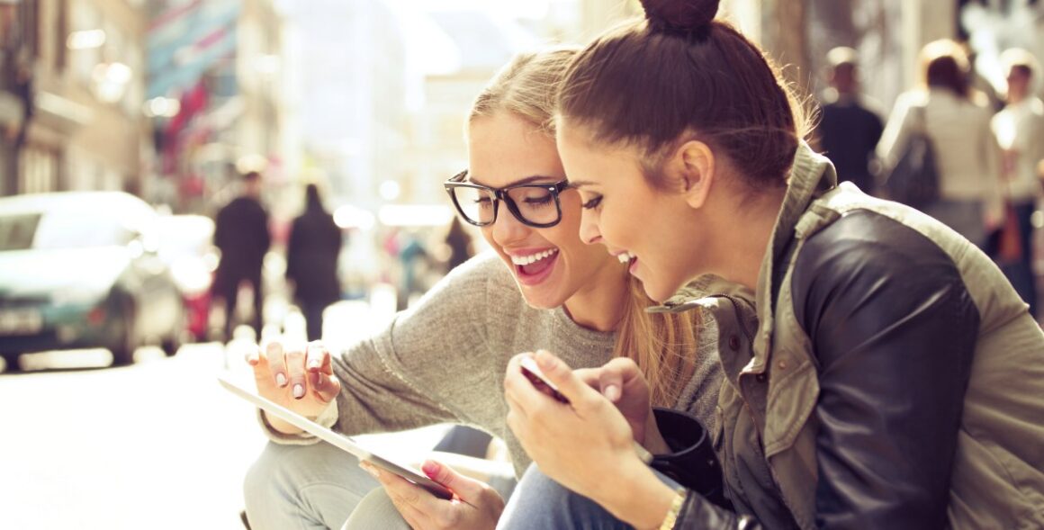 Lachende jungen Frauen blicken auf Tablet