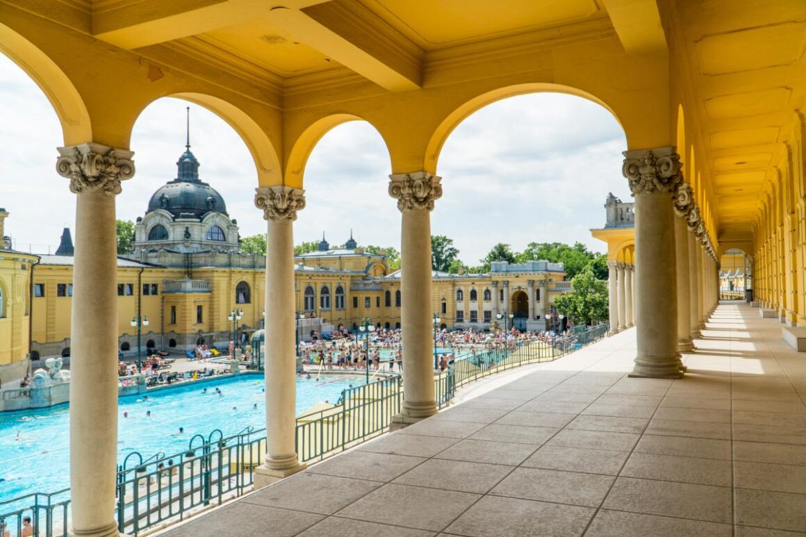 Szechenyi Thermalbad, Budapest: gelb gestrichenes Gewölbe und Säulen mit Schwimmbecken im Hintergrund