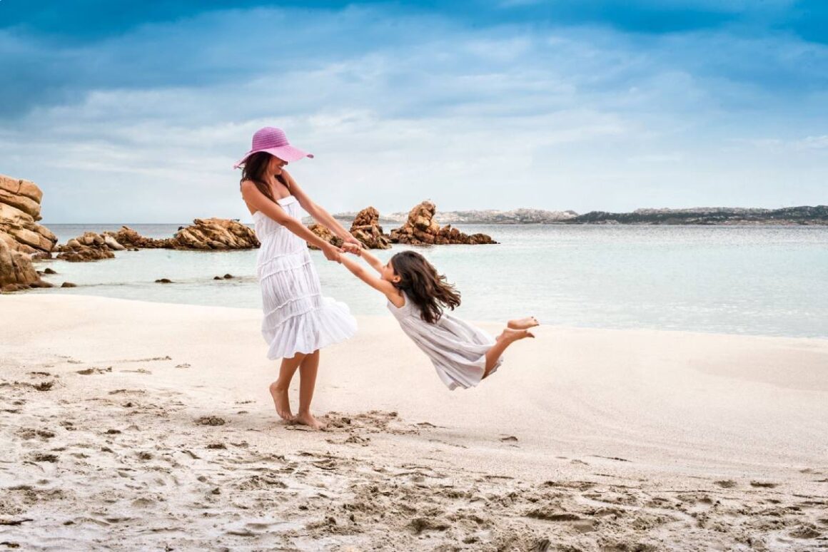Mutter schwingt fröhlich ihre Tochter am Strand von La Maddalena, Sardinien, Italien
