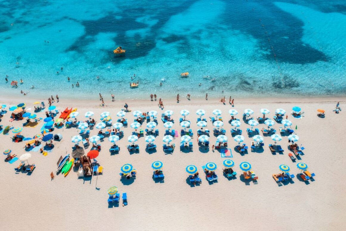 Bevölkerter Strand auf Sardinien mit Liegen und Sonnenschirmen in Vogelperspektive