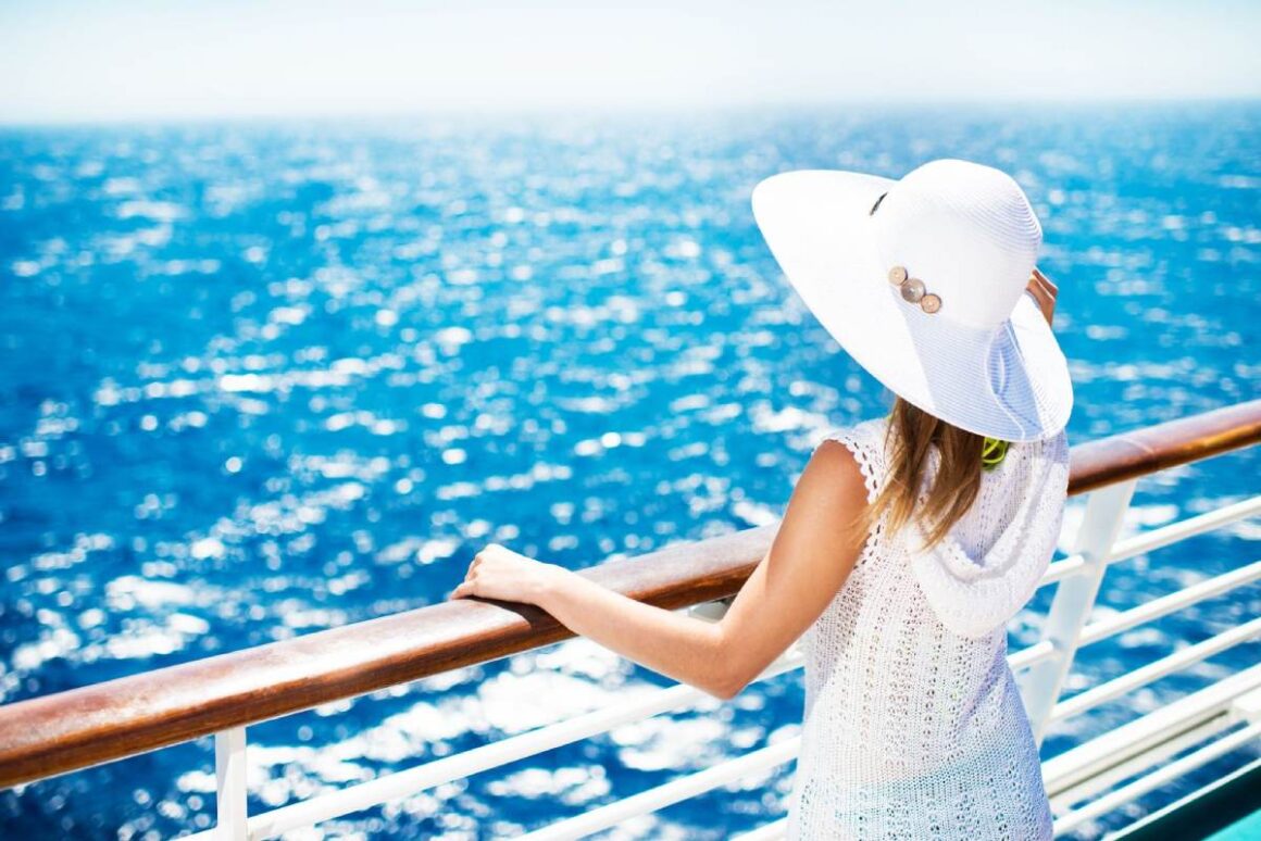 AIDA oder „Mein Schiff“? – Welcher Kreuzfahrtanbieter passt zu mir? Frau mit weißem Hut und weißem Kleid auf Schiff blickt auf Wasser
