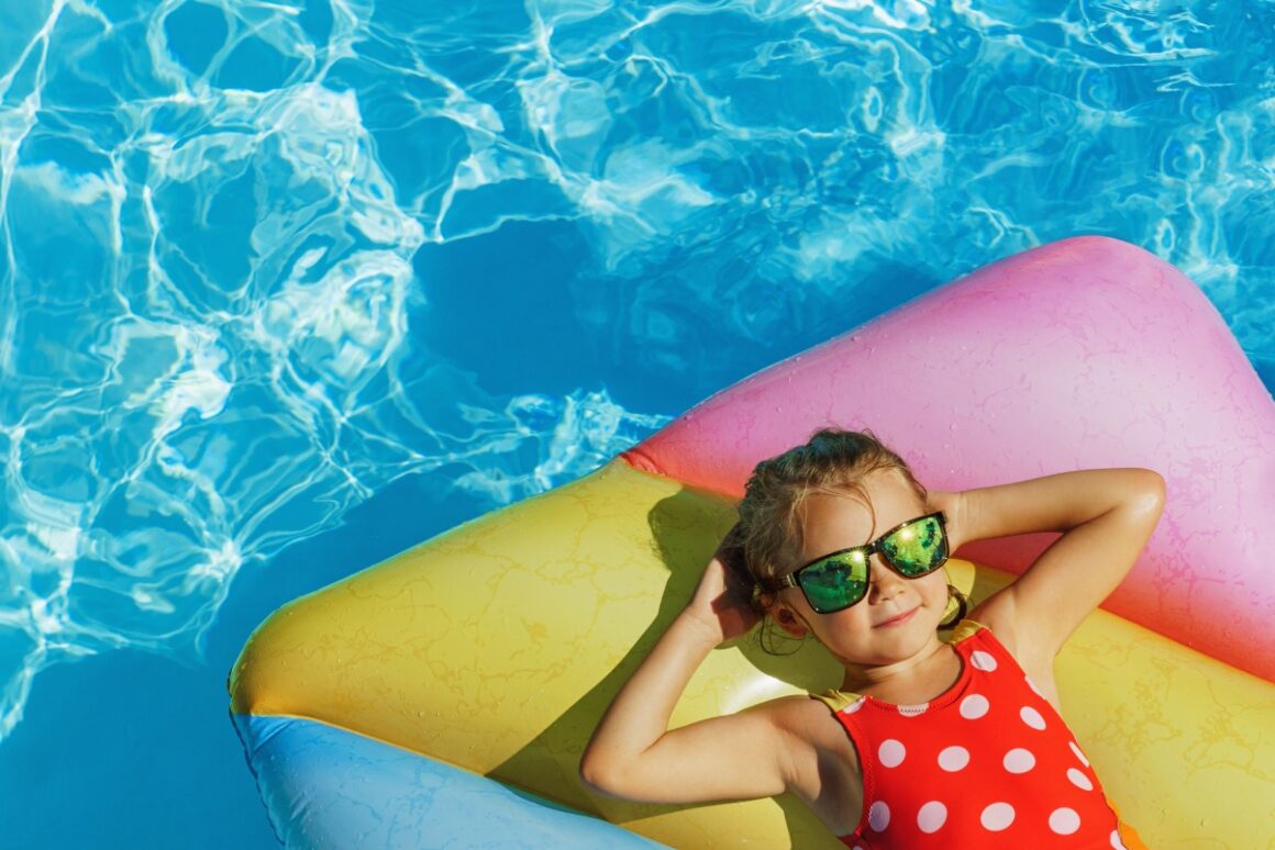Mädchen mit Sonnenbrille liegt auf Luftmatratze in einem Pool
