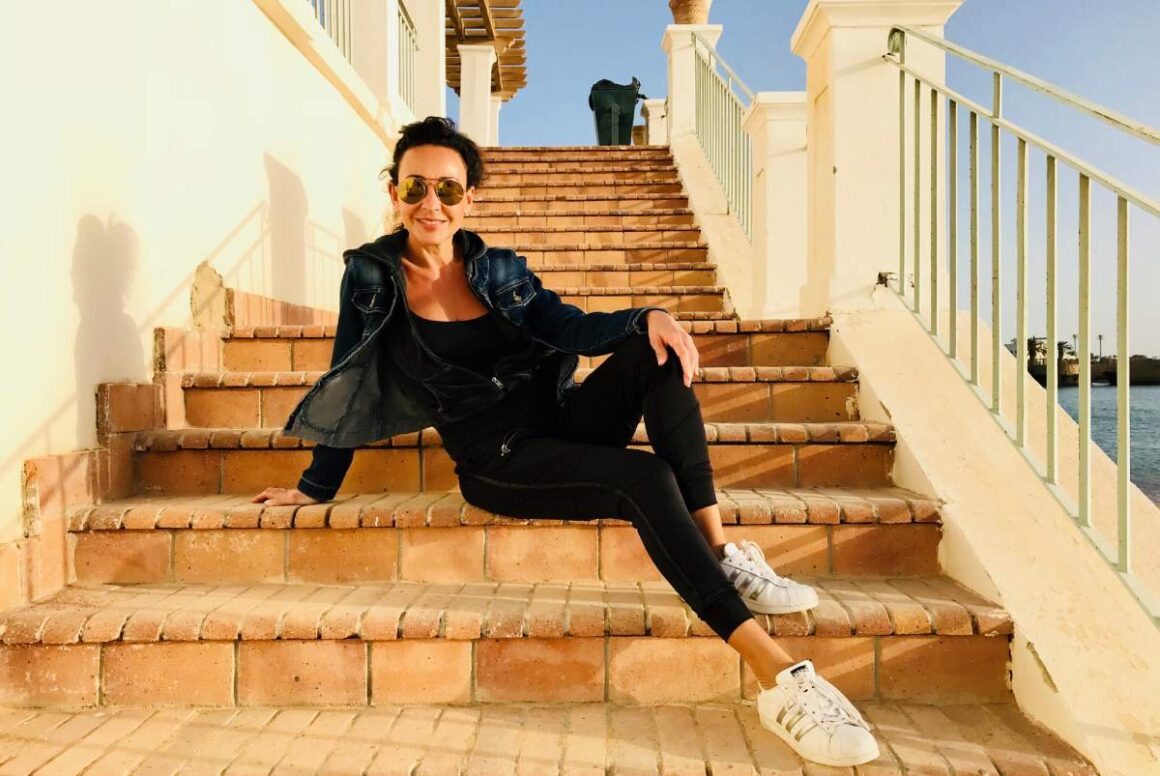 „Mein perfekter Urlaub beginnt, wenn der Handy-Akku leer ist.“ – Interview mit Moderatorin Mary Amiri Moderatorin Mary Amiri posiert auf einer Treppe
