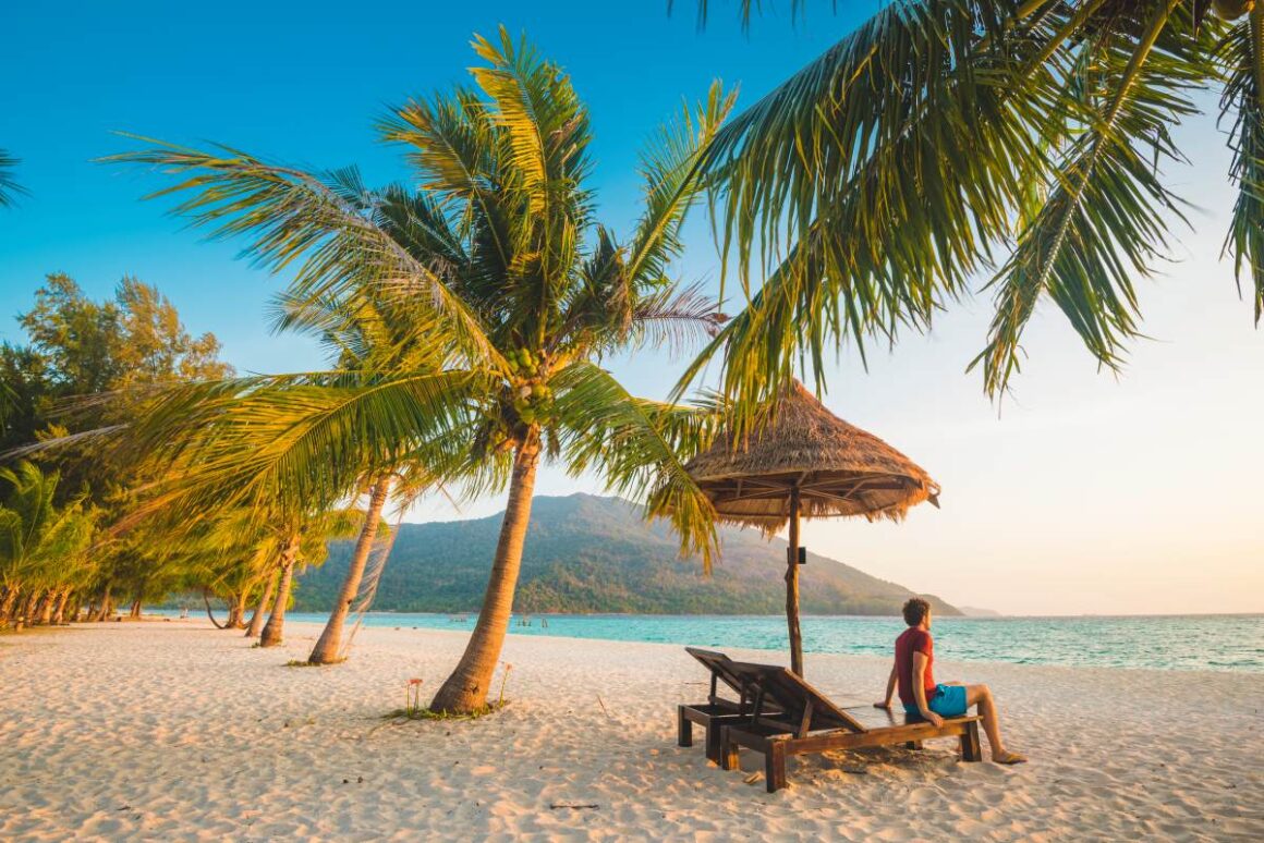 Mann auf Liege unter Palmen an Strand im Thailand
