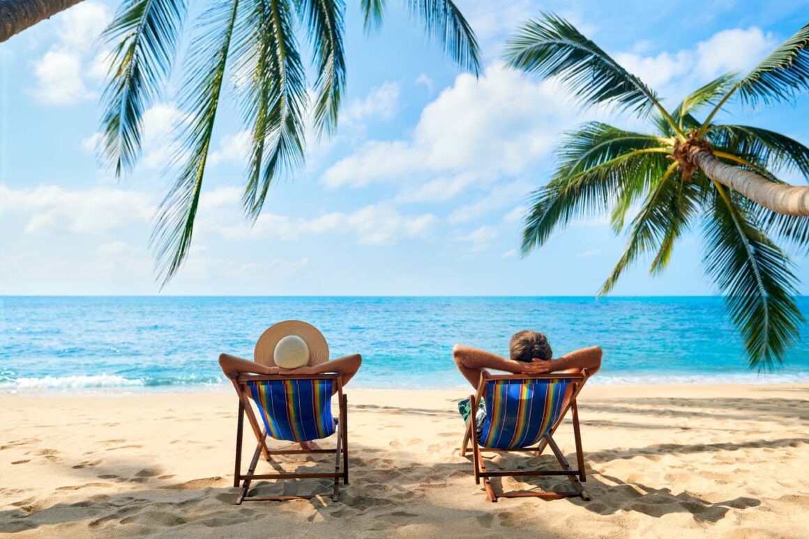 Wann solltet ihr euren Sommerurlaub buchen – Frühbucher oder Last-Minute? Paar in Liegestühlen am tropischen Palmenstrand