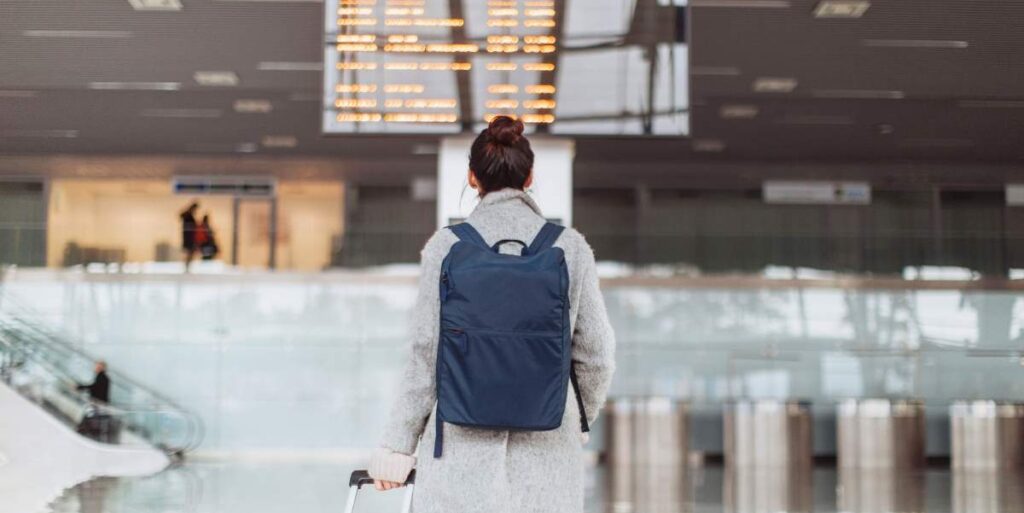 Frau am Flughafen mit Gepäck vor Infotafel mit Fluginfos