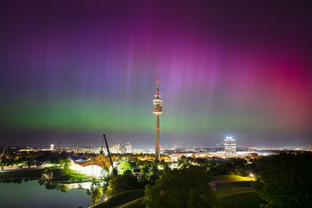 Polarlichter (schimmernde Grün- und Rosatöne) über der Skyline von München