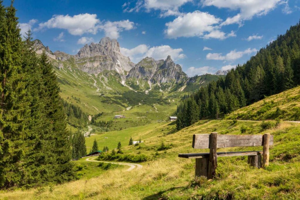Panoramablick auf die Alpen vom grünen Tal mit Holzbank