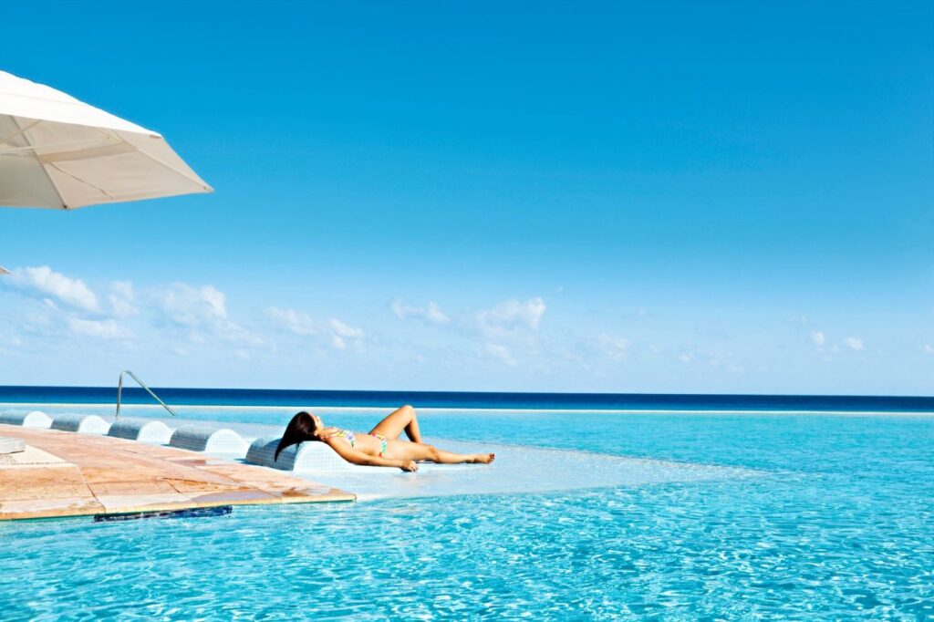 Paris-Syndrom: Diese Reiseziele enttäuschten Touristen 2025 am meisten Frau im Bikini sonnt sich vor Infinity Pool am Strand von Cancun, Mexiko