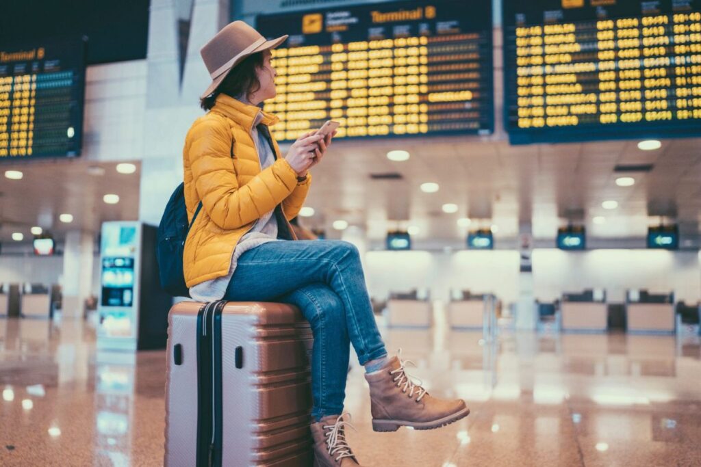 Italien: Weitere Streiks an Flughäfen geplant – ein Tag wird besonders kritisch Frau mit Gepäck am Flughafen schaut auf Abflugtafel