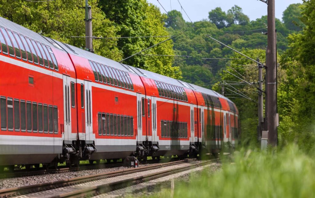 Warum Bahntickets bald teurer werden könnten Rote Regionalbahn der Deutschen Bahn auf Schienen mit Wald rund um den Zug