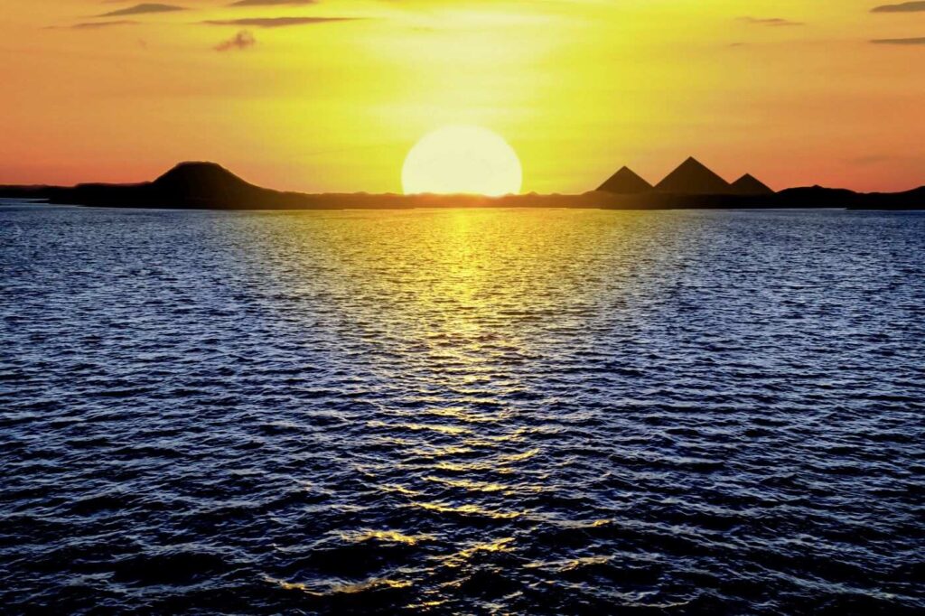 Sonnenuntergang bei den Pyramiden in Ägypten. Der gelbrot glühende Kugel wirft ein leuchtendes Band aufs Wasser im Vordergrund