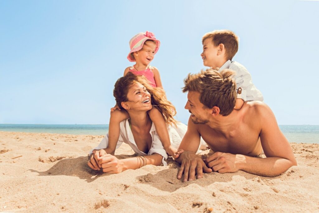 Diese Reise- und Freizeitanbieter sind besonders familienfreundlich Eine Familie mit zwei Kindern liegt an einem Strand bei blauem Himmel