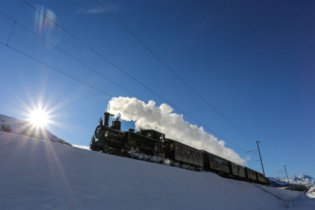 Dampflokzug fährt mit Waggons durch die verschneite Landschaft der Schweiz
