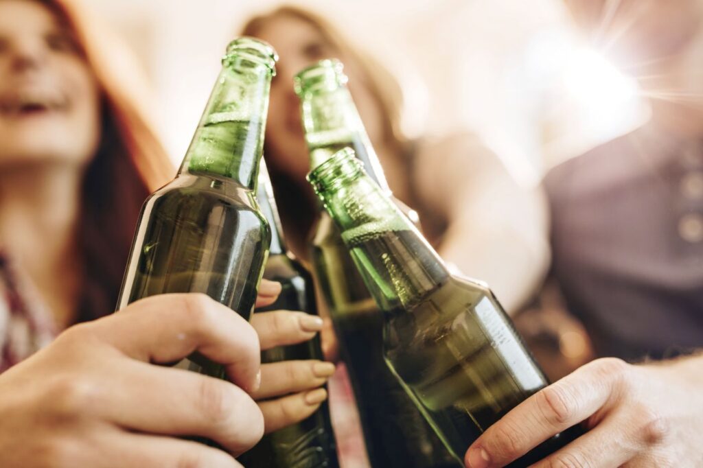 Alkoholverbot jetzt in allen deutschen Bahnhöfen: Was ist noch erlaubt und wo drohen Strafen? Nahaufnahme grüner Bierflaschen beim Anstoßen